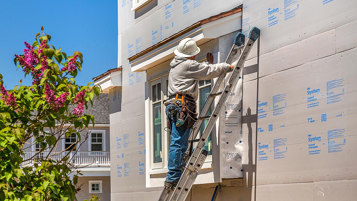 A man on a ladder installing continuous insulation