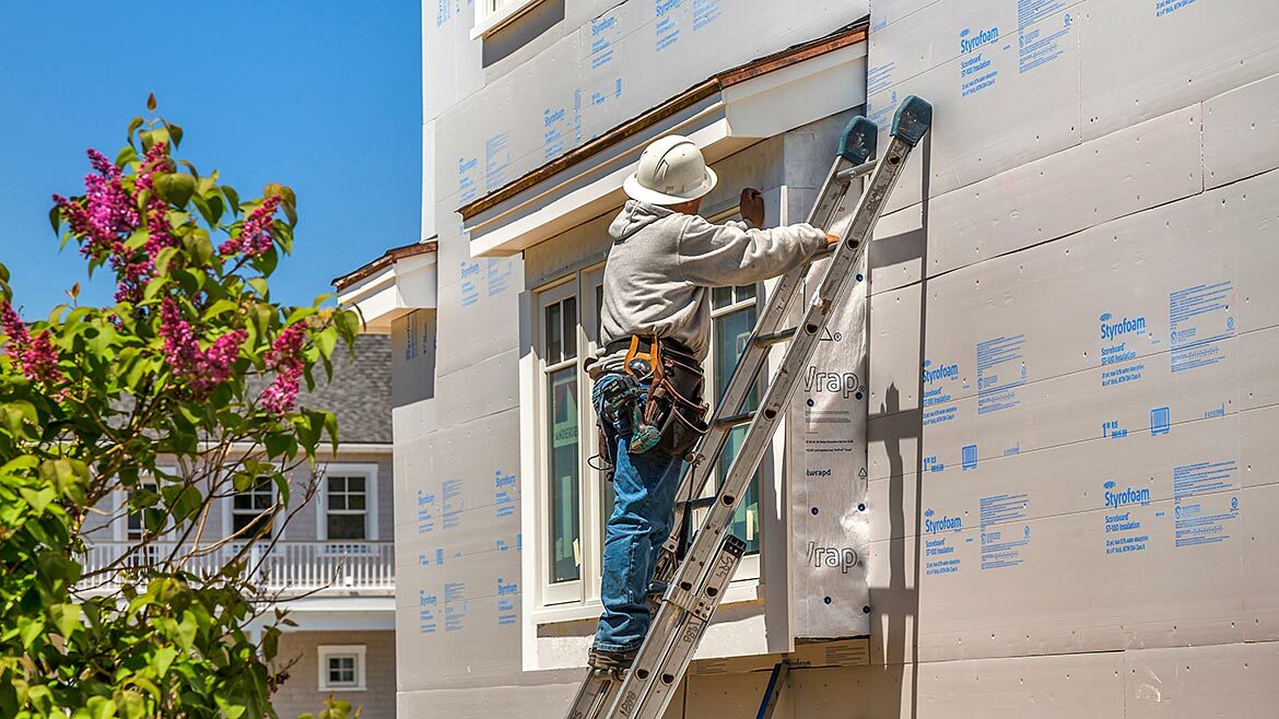 A man on a ladder installing continuous insulation